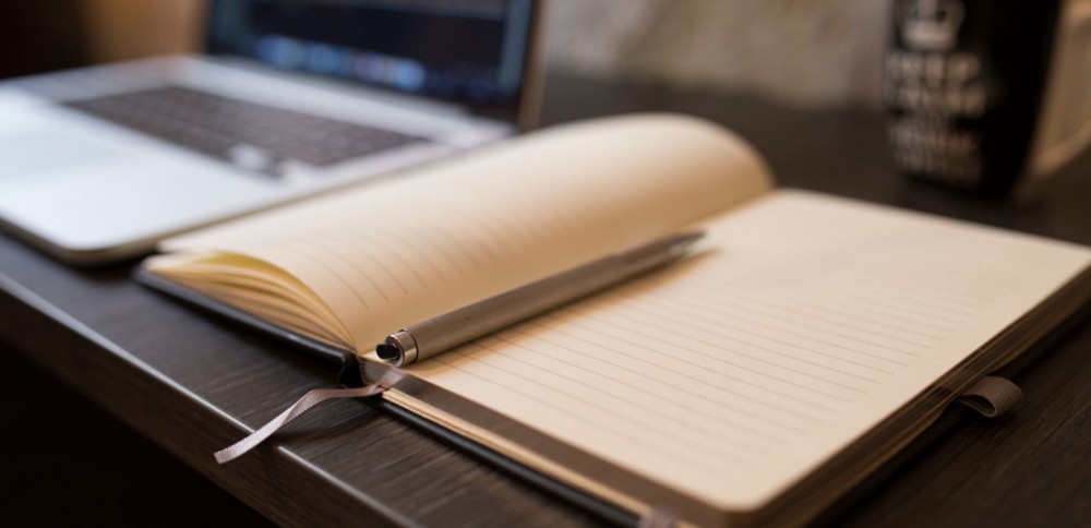 An empty notebook laying open next to a laptop. The laptop is in the background.