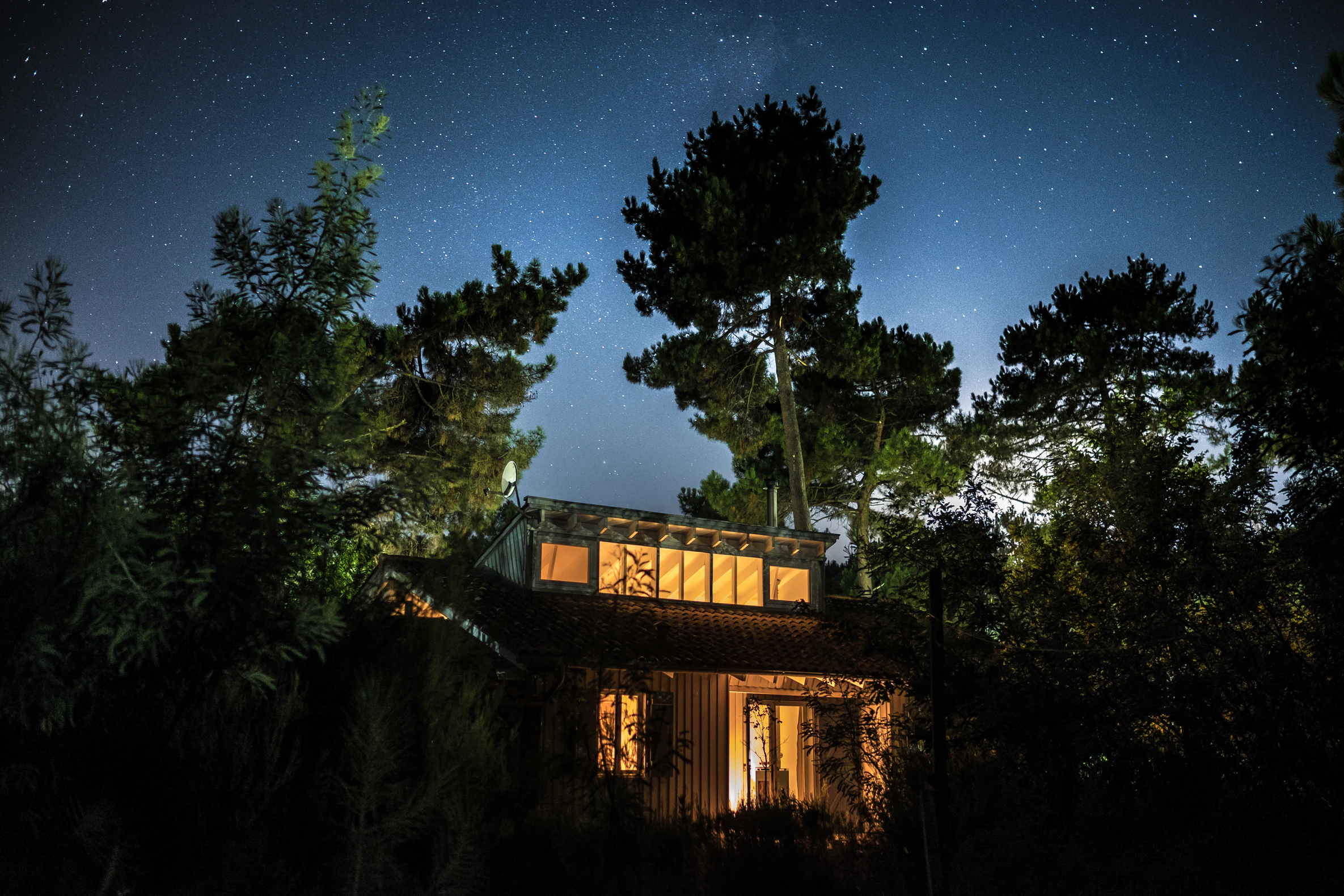 A house in the woods with the stars visible in the sky above.
